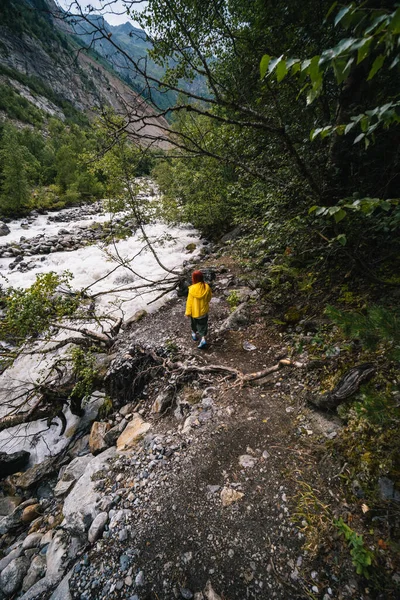 穿着黄色夹克的女人 游客徒步径直奔向查拉迪冰川 在波涛汹涌的背景下 佐治亚州的梅斯蒂亚河 旅行和度假的概念 垂直照片 — 图库照片