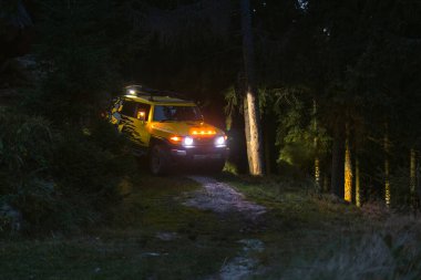 Bukovets, Ivano-Frankivsk, Ukrayna - 27 Ağustos 2022: Modifiye edilmiş bir Toyota FJ Cruiser aracı karanlık ormandan ayrılıyor, farlar yanıyor. Gece 4x4 Off-Road Yolu.