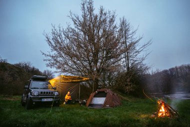 Khmelnytskyi, Ukrayna - 15 Nisan 2023: çatı rafı Niken ile Suzuki Jimny. Yağmurdan ve rüzgardan korunmak için. Çadır ve Şenlik Ateşi. duman seyahati ve aşırı, aktif eğlence.