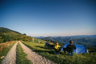 Bir çift motosikletli kadın ve erkek manzaranın tadını çıkarıyor. Sevgi dolu iki turist. İlişki ve macera kavramı. Tur motosikleti, çadır. Aktif yaşam tarzı. Katlanan sandalyeler. En yüksek dağlar. Ukrayna