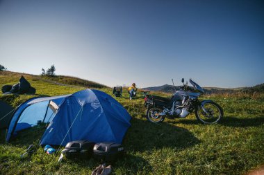 Kadın katlanır sandalyede tek başına oturuyor. Dağın tepesinde maceralı bir motosiklet turu. Kamp ekipmanları, off-road Jorney, seyahat çadırları. Ön görünüm