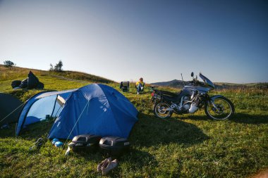 Kadın katlanır sandalyede tek başına oturuyor. Dağın tepesinde, turne motorsikletiyle. Kamp malzemeleri, Jorney yolu, seyahat çadırları. Yaz günü. Karpatlar Ukrayna Dağları
