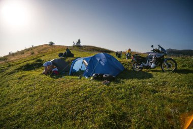 Kadın katlanır sandalyede tek başına oturuyor. Dağın tepesinde maceralı bir motosiklet turu. Kamp ekipmanları, off-road Jorney, seyahat çadırları. Ön görünüm