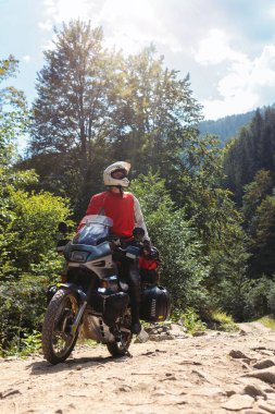 Motosikletli, beyaz kasklı, motosikletli bir erkek. Şehirlerarası tur motosikleti. Yan çantalar ve bavullar. Dağ yolu. Güneşli sıcak yaz günü. Aktif aşırı eğlence. Dikey fotoğraf.