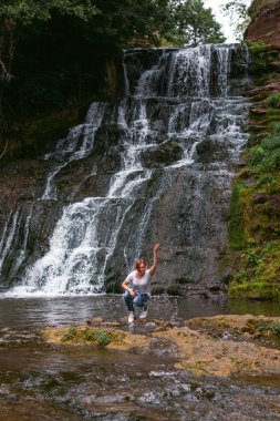 Genç kadın manzarası Dzhurynskyy şelalesiyle iyi eğlenceler. Kadın turist, turizm ve tatil, aktif yaşam tarzı. Chervonogorodsky. Dikey fotoğraf. Nyrkiv Ternopil Oblast Ukrayna