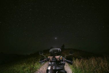 Birinci şahıstan görüntü. Motosiklet direksiyonu. Dağ toprak yolunun ortasında bir turist motosikletinde. Gece karanlık, yıldızlar parlıyor..