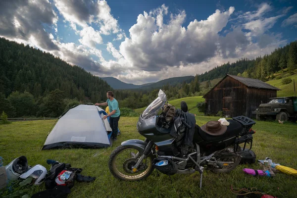 Dağların manzarası olan mavi bir çadır kuruyorum. Motosikletle bir gezi. Bir sürü teçhizatı olan bir tur motosikleti. Çantalar, bavullar. Birkaç motorcu, gece bir kampta durdular..