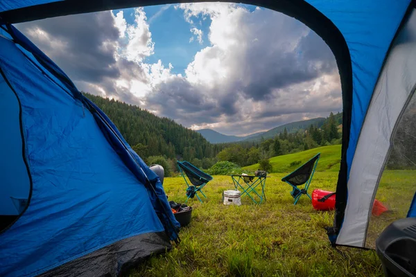 Turist çadırının içinden bak. Kamp gece için hazır. Taşınabilir sandalyeler, bir masa, dağ manzaralı bir akşam yemeği. Çam ormanı. Yaz günü. Uzayı kopyala Yürüyüş ekipmanları