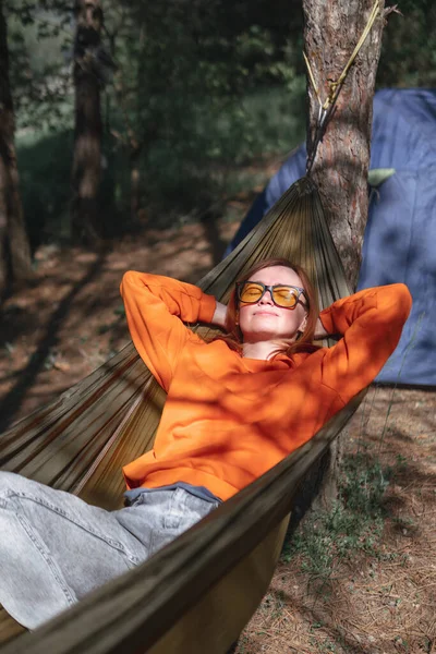Kamp yapan biri zeytin hamağında dinleniyor. Orman, yaz güneşli bir gün. Seyahat ve tatil. Dikey fotoğraf