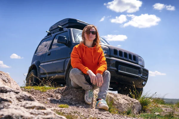 一个戴着太阳镜 穿着橙色毛衣的女人的画像 背景上有车架的越野车 旅行和冒险 积极的旅游业 山地活动 汽车旅行 — 图库照片