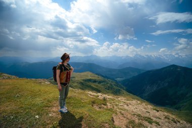 Geniş güneş şapkalı ve sırt çantalı bir kadın Koruldi Gölleri, Svaneti Bölgesi, Mestia Georgia 'ya yürüyüş rotasında bir turist. Seyahat ve aktif eğlence kavramı. Yaz günü