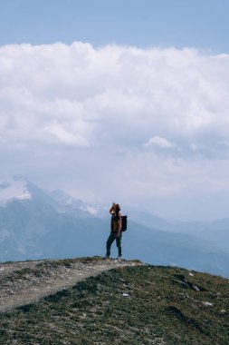 Geniş güneş şapkalı ve sırt çantalı bir kadın Koruldi Gölleri, Svaneti Bölgesi, Mestia Georgia 'ya yürüyüş rotasında bir turist. Seyahat ve aktif eğlence kavramı. Yaz günü. Dikey fotoğraf