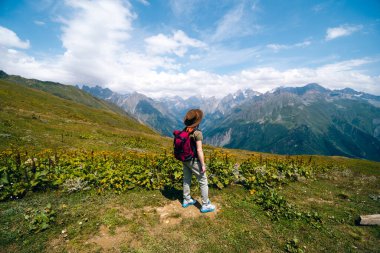 Geniş güneş şapkalı ve sırt çantalı bir kadın Koruldi Gölleri, Svaneti Bölgesi, Mestia Georgia 'ya yürüyüş rotasında bir turist. Seyahat ve aktif eğlence kavramı. Yaz günü
