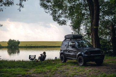 Kız katlanır bir sandalyede oturuyor. Piknik. Gölün kıyısındaki off-road aracı, çölün ortasındaki orman. Tanınmadan. Bir SUV aracında aşırı eğlence kavramı