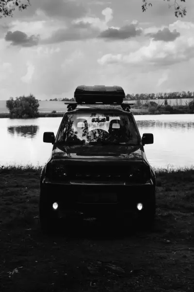黑人和白人 湖岸上一辆越野车的轮廓 停在森林里 前灯没有得到承认 越野车上的极端娱乐的概念 垂直照片 — 图库照片