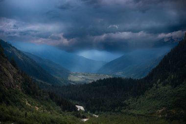 Uzak manzara, yüksek Kafkas dağlarının arasındaki vadi, yaz akşamı, dramatik yağmur bulutları. Shdugra Şelalesi, Mazeri, Svaneti, Georgia