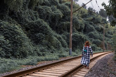 Demiryolu boyunca şapkalı bir kadın yürüyor. Vahşi bir sahil ortancasına giden tehlikeli bir yol. Sulu yeşil çalılıklar, uzayı kopyalayın. Yaz günü. Tsikhisdziri Georgia