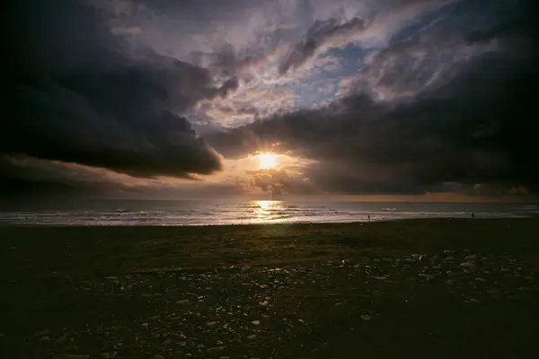 Sunset view, seashore, stormy waves, heavy rain clouds on horizon, sun breaking through the cloud like an eye