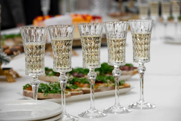 buffet table, white tablecloth, champagne glasses on a long stem. Carbonated white wine. Selective focus, plates and snacks. The concept of a coffee break for corporate parties and events.