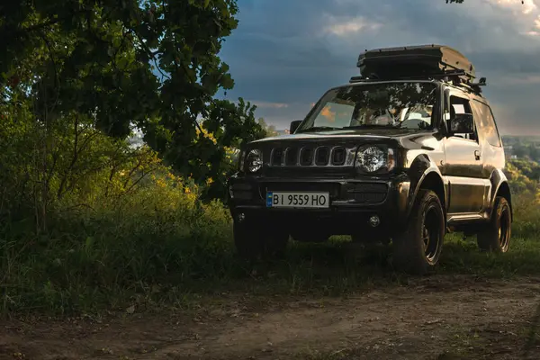 stock image Khmelnytskyi, Ukraine - august. 11. 2024: Old Jb43 Suzuki Jimny 2010 outdoor. Roof rack. an off-road vehicle is parked at a forest. Summer evening, shade among the trees. recreation and tourism.