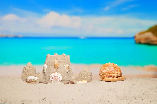 stock image Sand castle and sea shell on sand beach at tropical resort. Family vacation. Relax on the beautiful sea coast beach. Azure water on the ocean, sea coast resort. Summer holidays. Blue sky. Copy space.