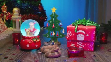 Yılan - Çin Ay takviminde 2025 Yılın Sembolü. Noel hediyesi kutusu, Noel ağacı, Noel Baba ile cam kar küresi, kırmızı mumlar..