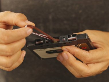 This image shows a person's hand manipulating a cassette tape, specifically the magnetic tape protruding from the cartridge.
