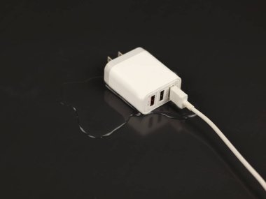 Image of a USB-C charger immersed in a small puddle of water.