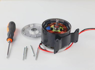 Close-up of a partially disassembled electric motor, revealing the internal copper coils and rotor. A screwdriver and various screws are placed next to the motor.