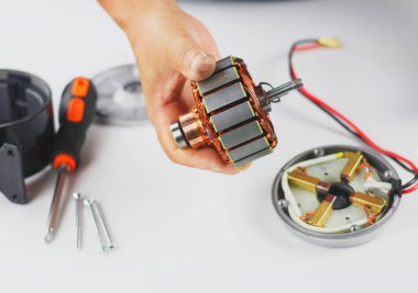 This image shows the disassembly or repair of an electric motor, likely from an electrical appliance or small machine. The rotor (armature) with copper windings and a laminated core is shown in a hand.