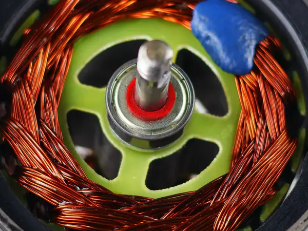 A close-up view of the stator of an electric motor, featuring a wound copper coil and a central bearing. The bright orange copper wires contrast with the metallic silver.