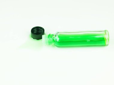 A clear glass bottle containing bright green liquid lies sideways next to a removed black cap.