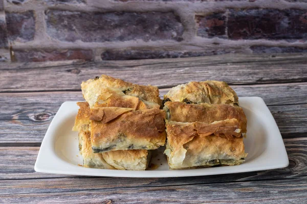 Turkish pastry with spinach and cheese on a white plate. A traditional Turkish pastry, roll pastry. Spinach and cheese pie on a wooden table.