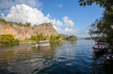 The rock-cut temple tombs of the ancient city of Kaunos in Dalyan, Mula, Turkey. Beautiful view of Dalyan river with reed beds, excursion boats and carved tombs in the background.