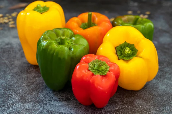 Yellow , red , green colored bell peppers on gray background .