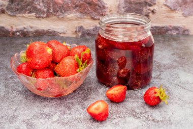 Ev yapımı lezzetli çilek reçeli ve ahşap bir masada çilek.