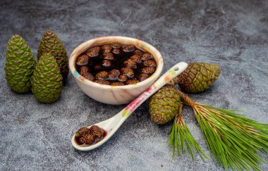 Young pine cones jam , molasses in glass bowl on gray marble background . Delicious jam with small pine cones, molasses.