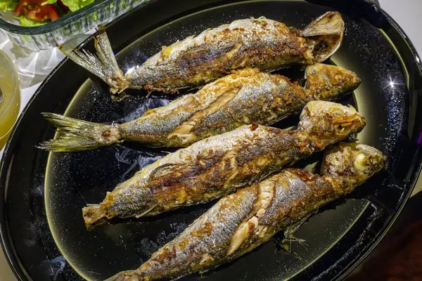Fried fishes on black dish. top view