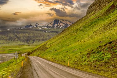Toprak yol, karlı dağlar ve İzlanda 'da gün batımı.