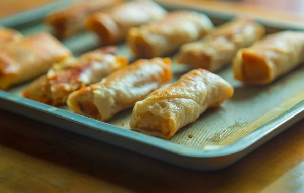 Freshly cooked spring rolls are arranged on a baking sheet. Spring rolls fried in cooking oil. The exterior looks golden and crispy, and the texture is crispy on the outside and tender on the inside. It is a very delicious family snack.