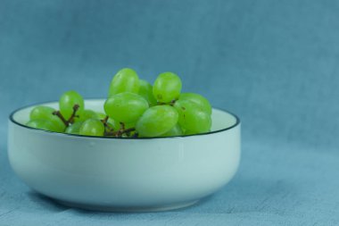 Taze yeşil üzümler beyaz bir seramik kasede sağlam bir arka planda. Yaz ve sonbahar meyveleri lezzetlidir..