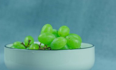 Beyaz bir porselen kasede taze yeşil üzümler. Görüntü, yeşil üzümlerin bir kısmını gösteriyor. Lezzetli üzümler