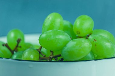 Beyaz bir porselen kasede taze yeşil üzümler. Görüntü, yeşil üzümlerin bir kısmını gösteriyor. Lezzetli üzümler