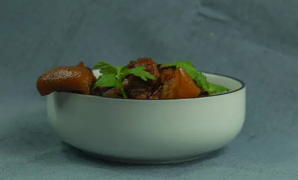 The shot shows a traditional Chinese home cooked dish, braised pork. The white porcelain bowl is in the center focus of the image and contains braised pork topped with tender green cilantro leaves. Individual preparation of a home-cooked dish.