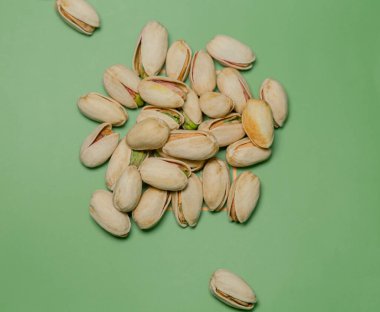 Görüntü yeşil bir zemin üzerine serilmiş bir şam fıstığı yığınını gösteriyor. Fındıkların doğal dokusunu ve rengini vurguluyor. Pistachios 'un soluk sarı bir kabuğu var ve bazı açıkları parlak yeşil çekirdekleri gösteriyor.