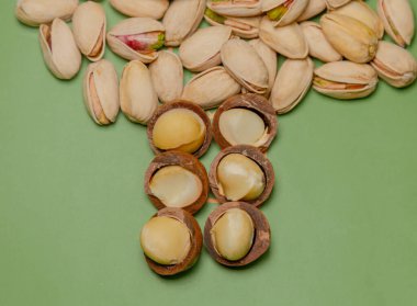 Yeşil arka planda, çerez yığınları: makadamialar ve şam fıstıkları. Bu fındıklar olgun, et dolu ve lezzetli bir tadı var. Protein açısından zengin olan bu fındıklar doymamış yağ ve diyet lifleri.