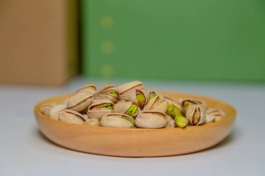 Resim yeşil bir arkaplan ve beyaz bir masanın üstüne yerleştirilmiş ahşap bir tepsiyi gösteriyor. Ahşap tabak fıstıklı çerezlerle dolu. Bu sağlıklı bir çerez ve en sevdiği sağlıklı yiyecektir..