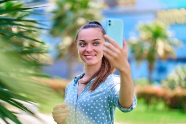 Genç bir kadın dışarıda akıllı telefondan kendi fotoğrafını çekiyor. Dijital hareketlilik yaşam tarzına sahip modern insanlar  
