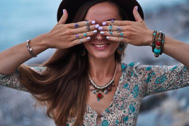 Manikürlü, takı aksesuarlı, keçeli şapkalı ve elbiseli mutlu özgür kadın. Boho detayı kapat