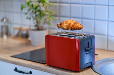 Modern kırmızı tost makinesi kahverengi tatlı kruvasanı ısıtır.